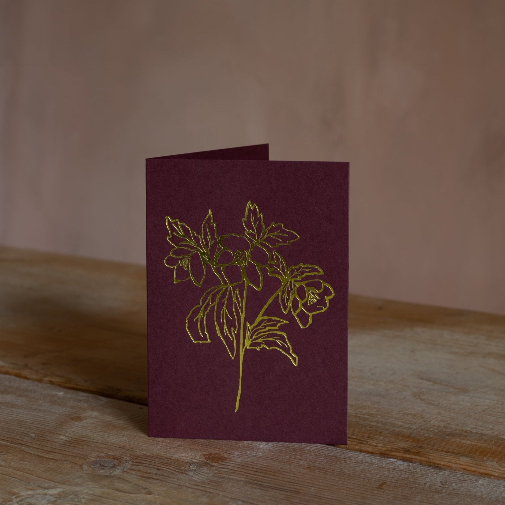 Elegant Christmas rose greeting card with a minimalist gold line illustration on deep red cardstock, perfect for holiday wishes.