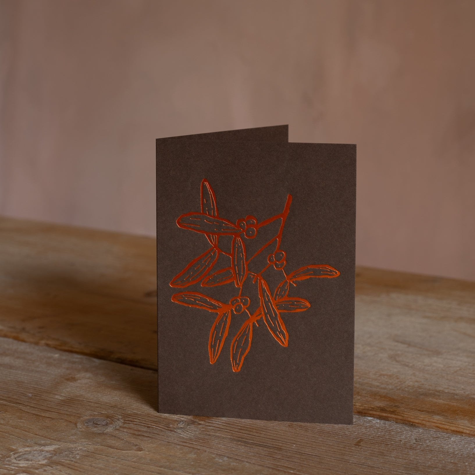 Charming mistletoe greeting card featuring a simple orange line illustration on brown cardstock, ideal for festive holiday messages.