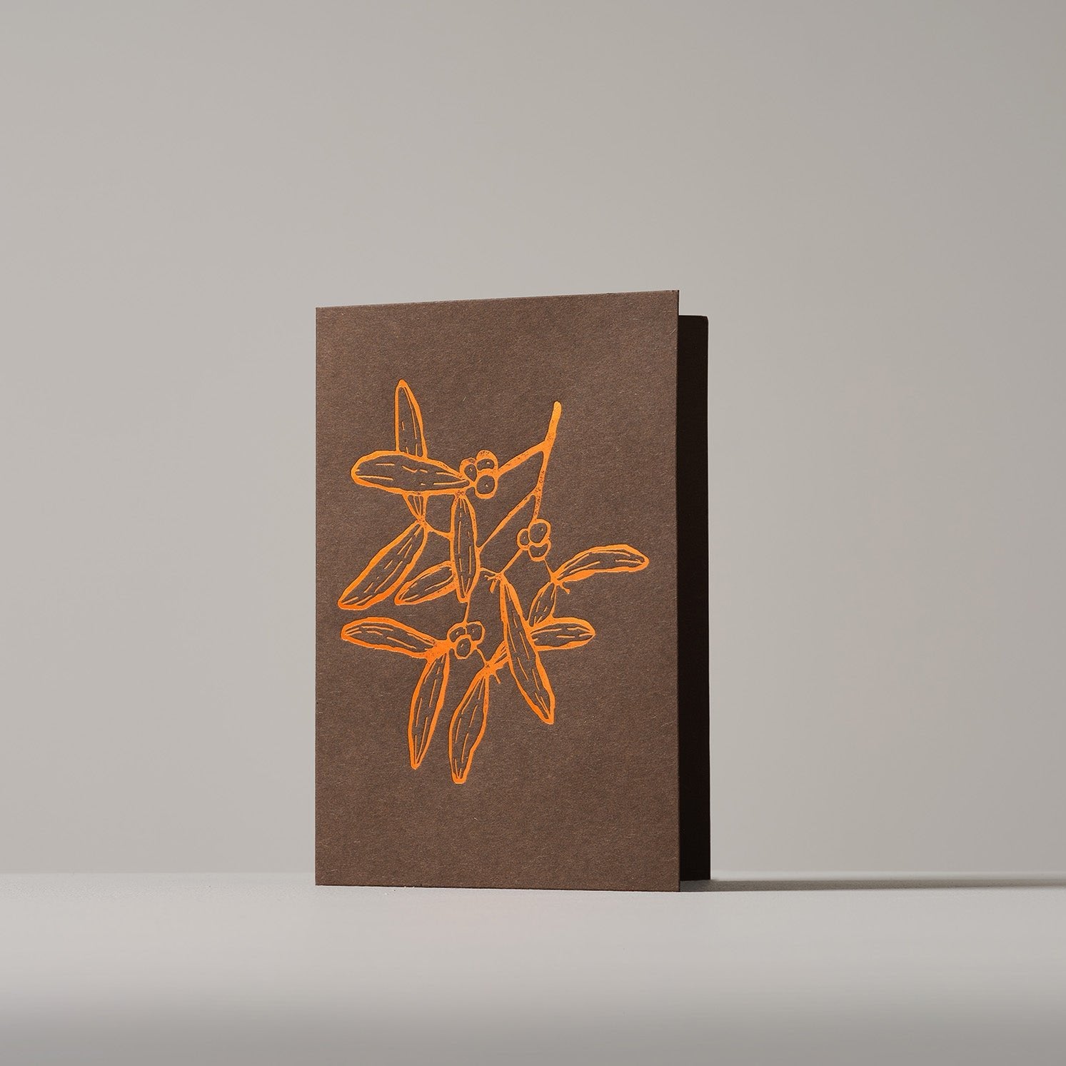 Christmas card featuring a copper-outlined mistletoe  on a wintery Brown background, standing on a neutral surface.